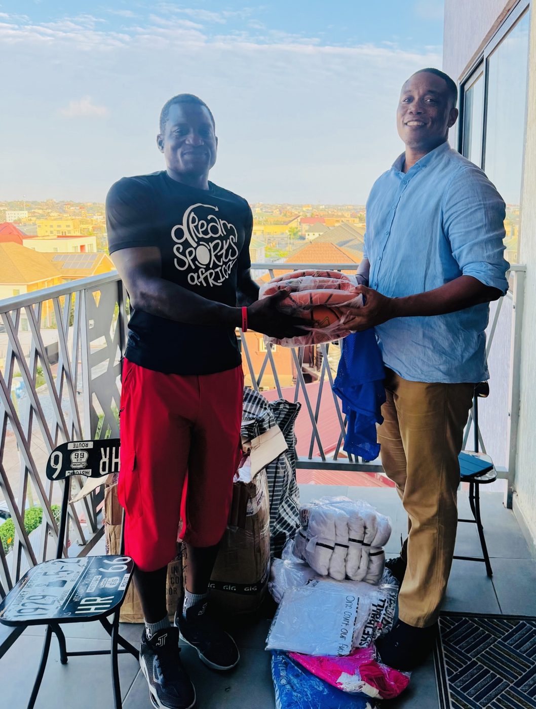 Sports supplies handoff in Accra, 2026: a person in a Dream Sports Africa T-shirt hands bagged basketballs to a DC Dynamics representative