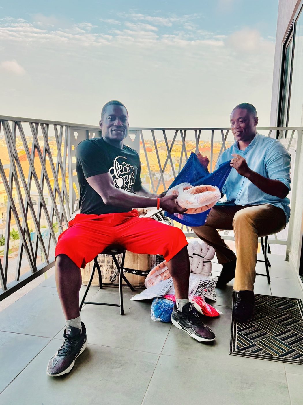 Sports supplies handoff in Accra, 2026: a person in a Dream Sports Africa T-shirt and a DC Dynamics representative sorting basketballs and a training bib